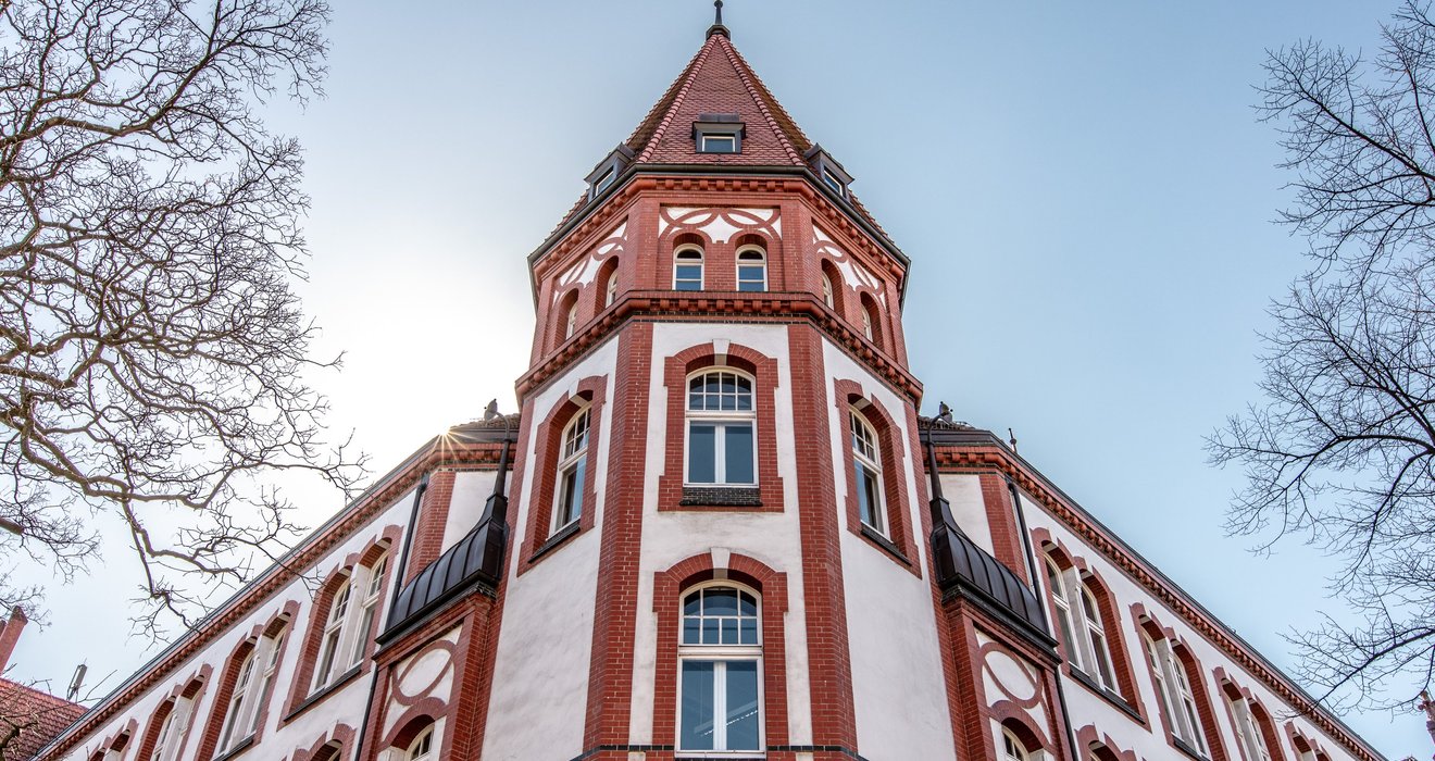 Das IFSH Hauptgebäude - Ein rot-weißes Fachwerkgebäude mit einem spitzen Turm, von unten gesehen.